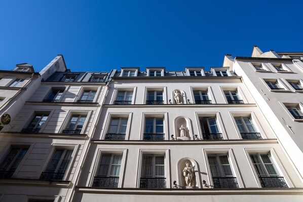 A multi-story building with classical architecture, featuring symmetrical windows and statues on the facade.