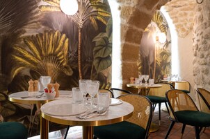 Un interior de restaurante con mesas redondas, sillas tapizadas en verde y un mural de hojas tropicales en la pared.