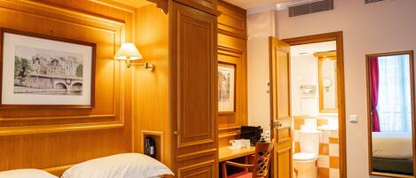 A hotel room with a bed, a desk, a chair, a bathroom, and wooden paneling.