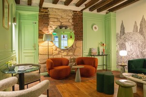Una habitación con paredes verdes, una pared de piedra, sillones anaranjados, una mesa de ajedrez y un sofá verde.