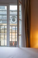 Habitación de hotel con un ventanal grande, una cama y vistas a un edificio de arquitectura clásica.