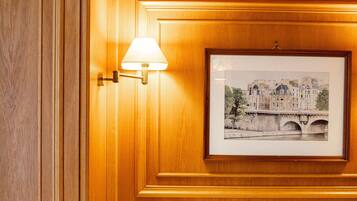 A hotel room with a wooden paneled wall, a framed picture of a bridge, and a bed with white linens.