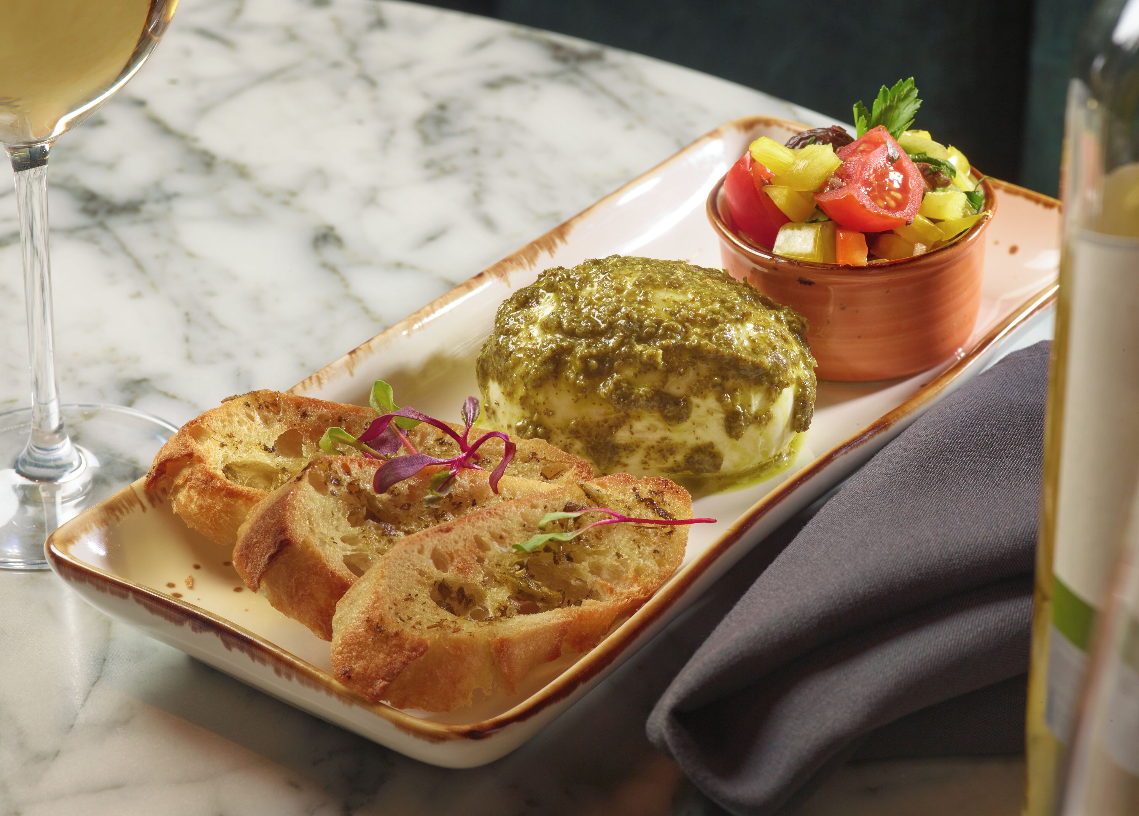 A plate with bread, a green sauce-covered item, and a fruit salad on a marble table.