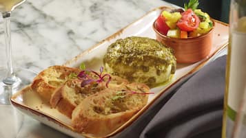 A plate with bread, a green sauce-covered item, and a fruit salad on a marble table.