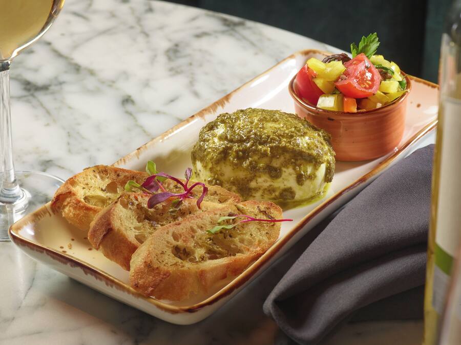 A plate with bread, a green sauce-covered item, and a fruit salad on a marble table.