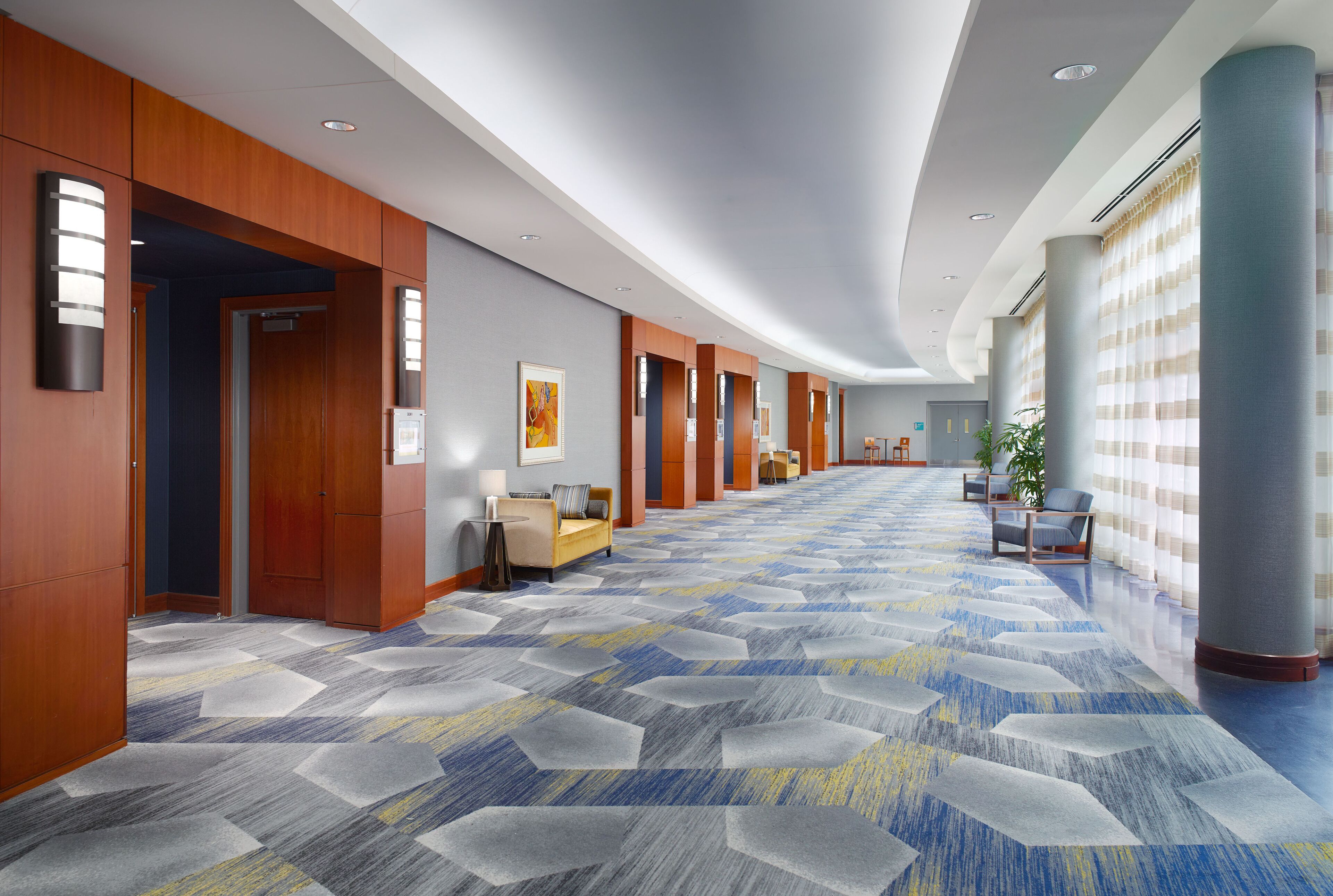 Un couloir d’hôtel avec des boiseries, une moquette à motifs et des espaces aménagés pour s’asseoir.