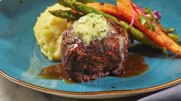 A plate with a steak topped with a creamy sauce, accompanied by mashed potatoes and roasted vegetables.