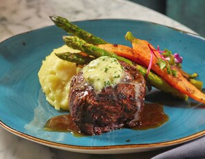A plate with a steak topped with a creamy sauce, accompanied by mashed potatoes and roasted vegetables.