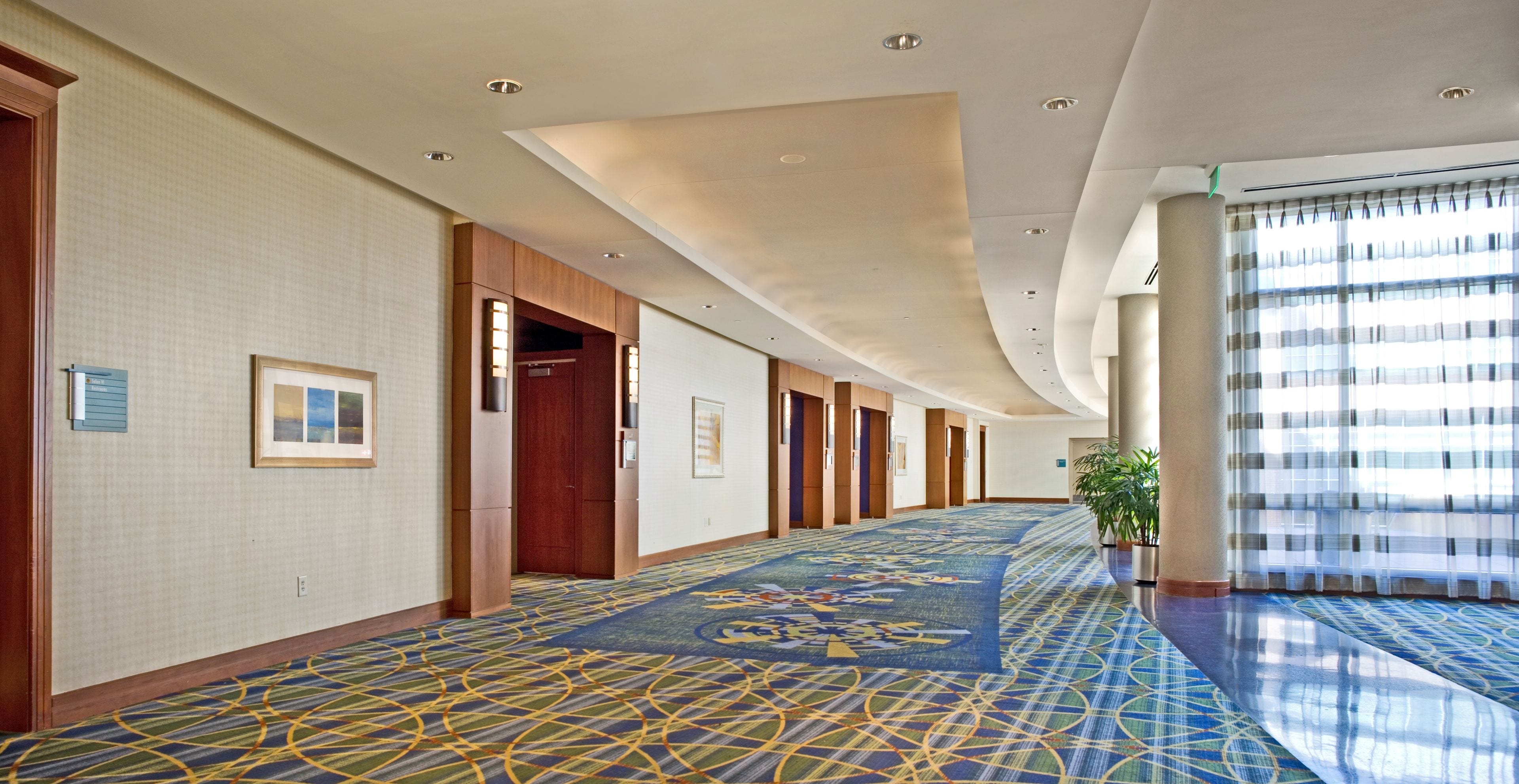 A hotel corridor with a patterned carpet, wooden doors, and framed pictures on the walls.