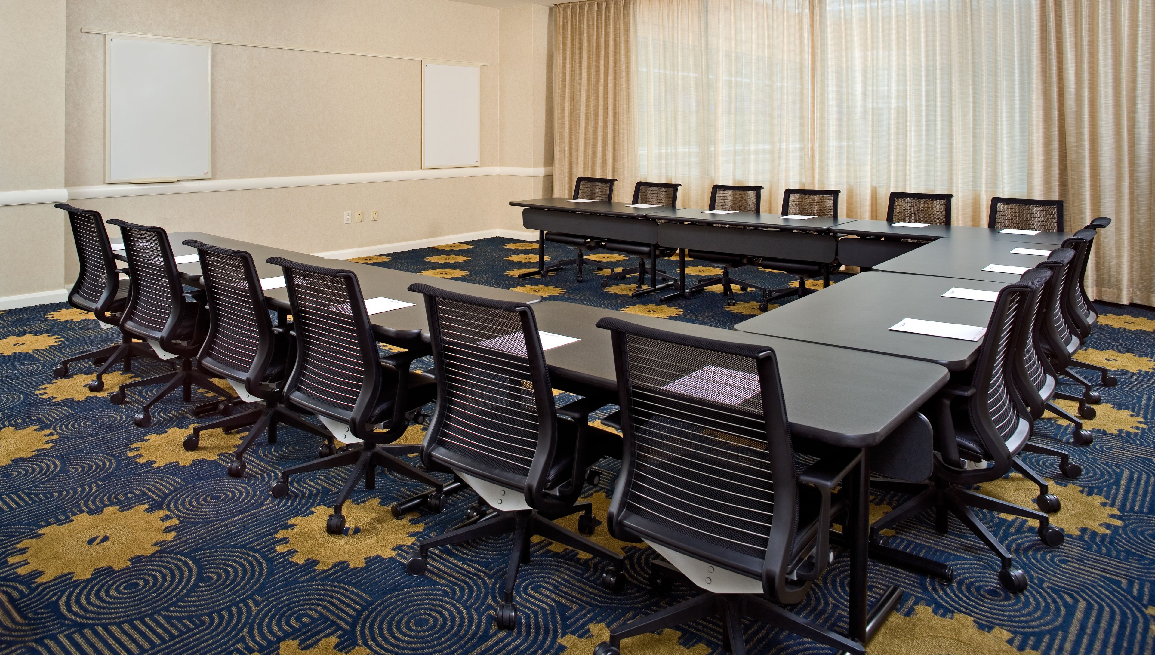 A conference room with a long table, multiple chairs, and a carpeted floor.