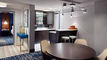 A modern hotel room with a dining area, a kitchen, and a bathroom.