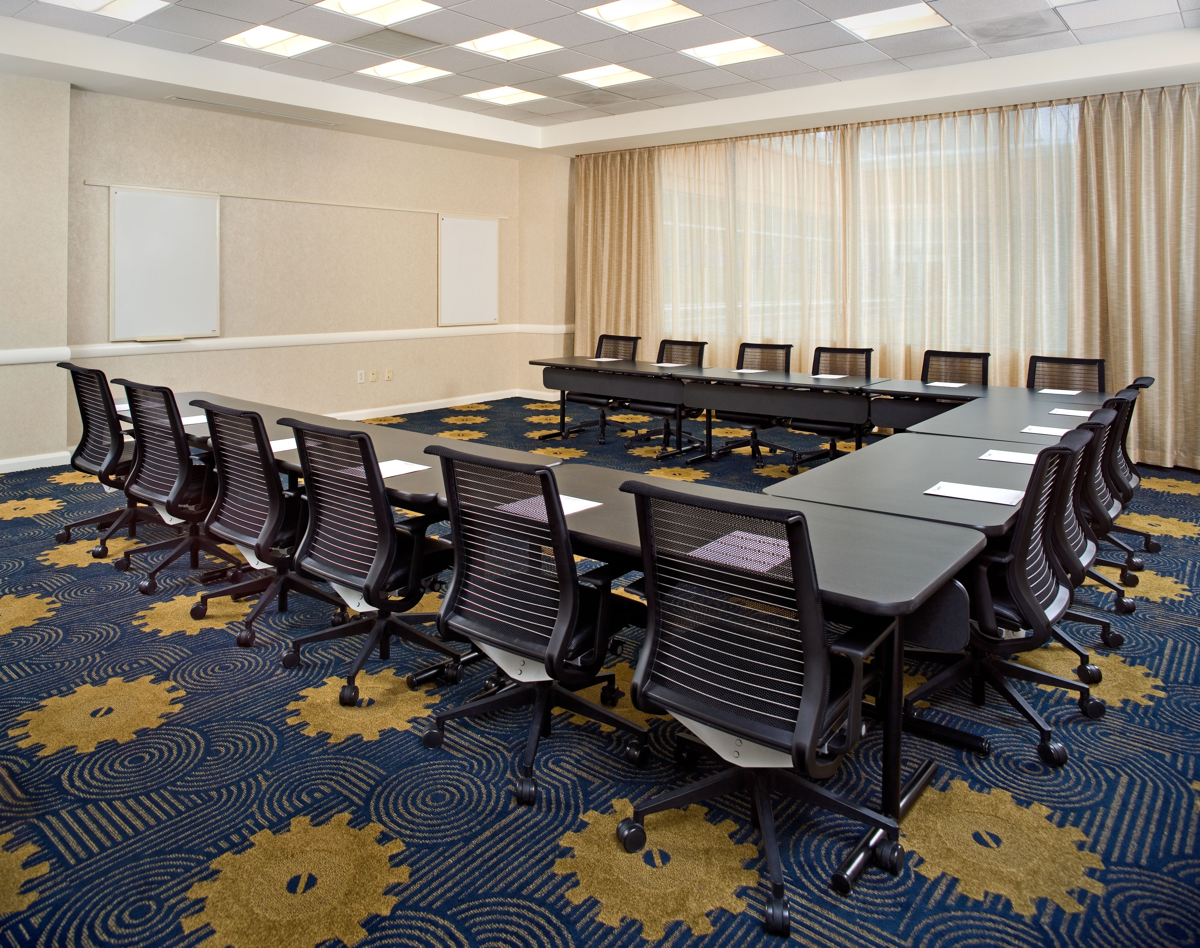 A conference room with a long table, multiple chairs, a whiteboard, and a patterned carpet.