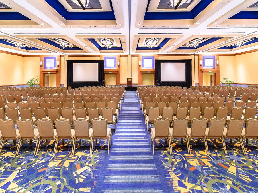 Une salle de conférence avec des rangées de chaises, une moquette bleue et une scène à l’avant.