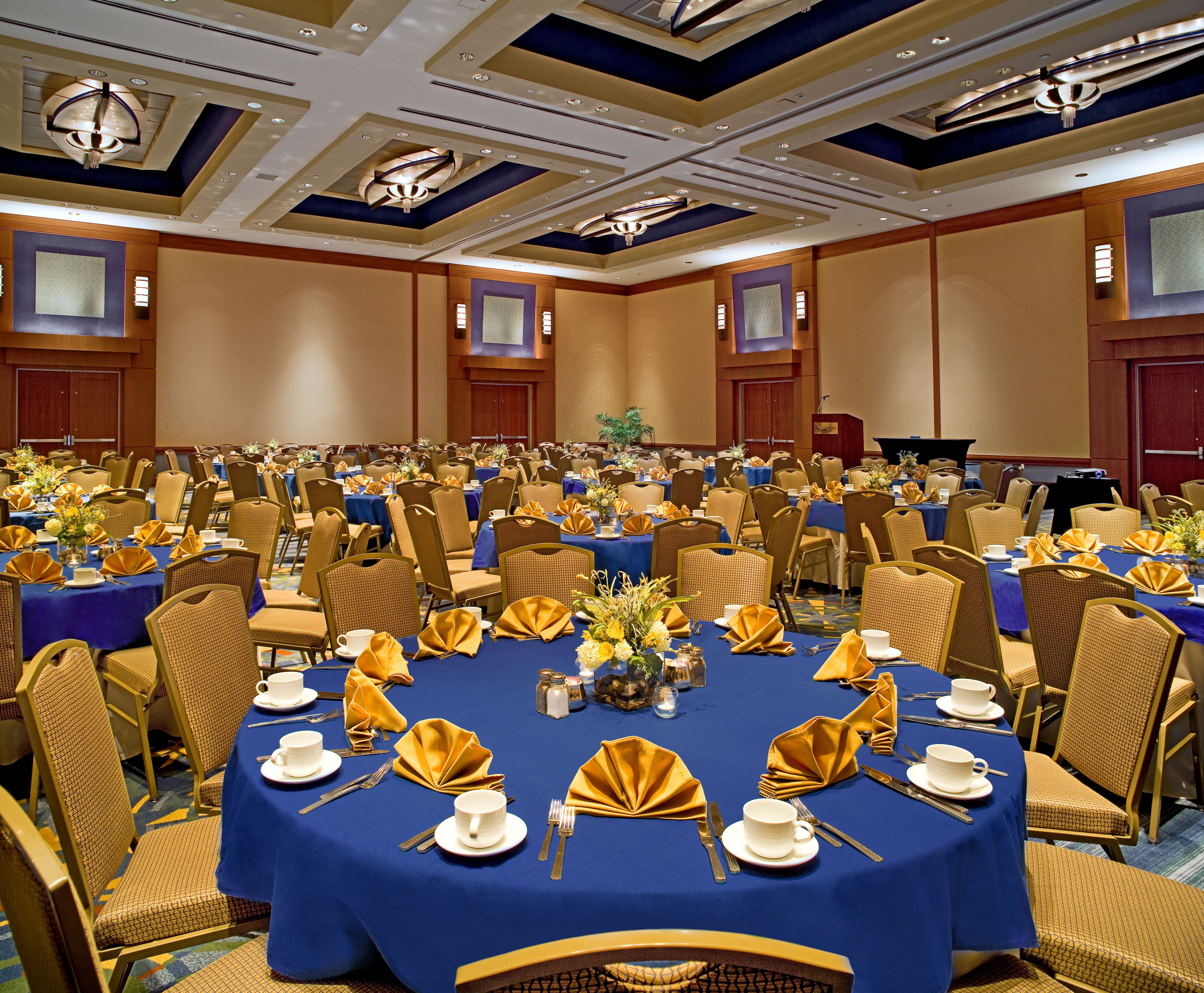 A banquet hall with round tables set for dining, equipped with gold napkins, white plates, and cutlery.