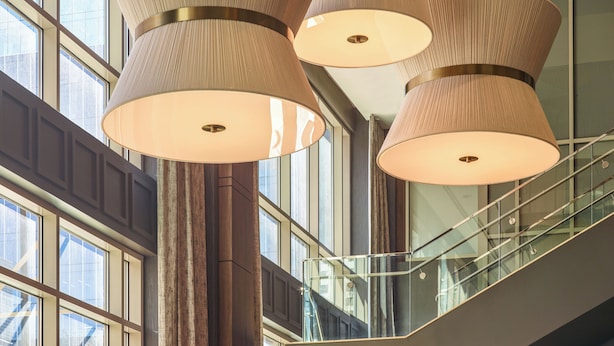 Un interior modern amb grans finestres, una escala i diverses làmpades penjants.