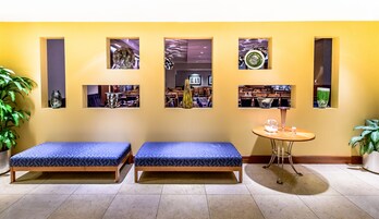 Une pièce avec deux lits recouverts de coussins bleus, une petite table ronde ornée d’un vase et d’une bougie, et trois tableaux encadrés accrochés au mur.