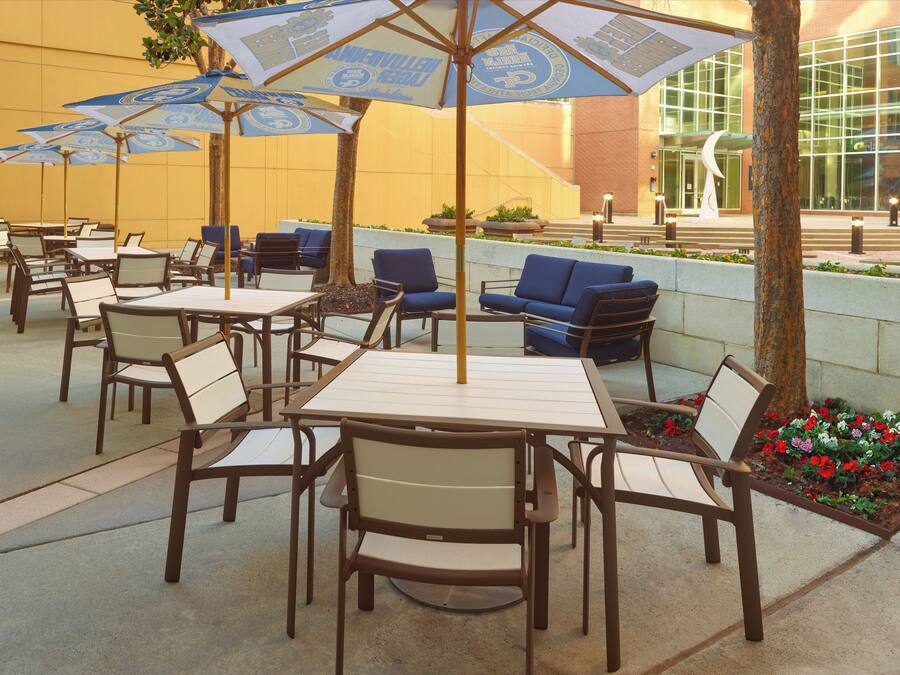 Outdoor seating with tables and chairs, umbrellas, and a building in the background.
