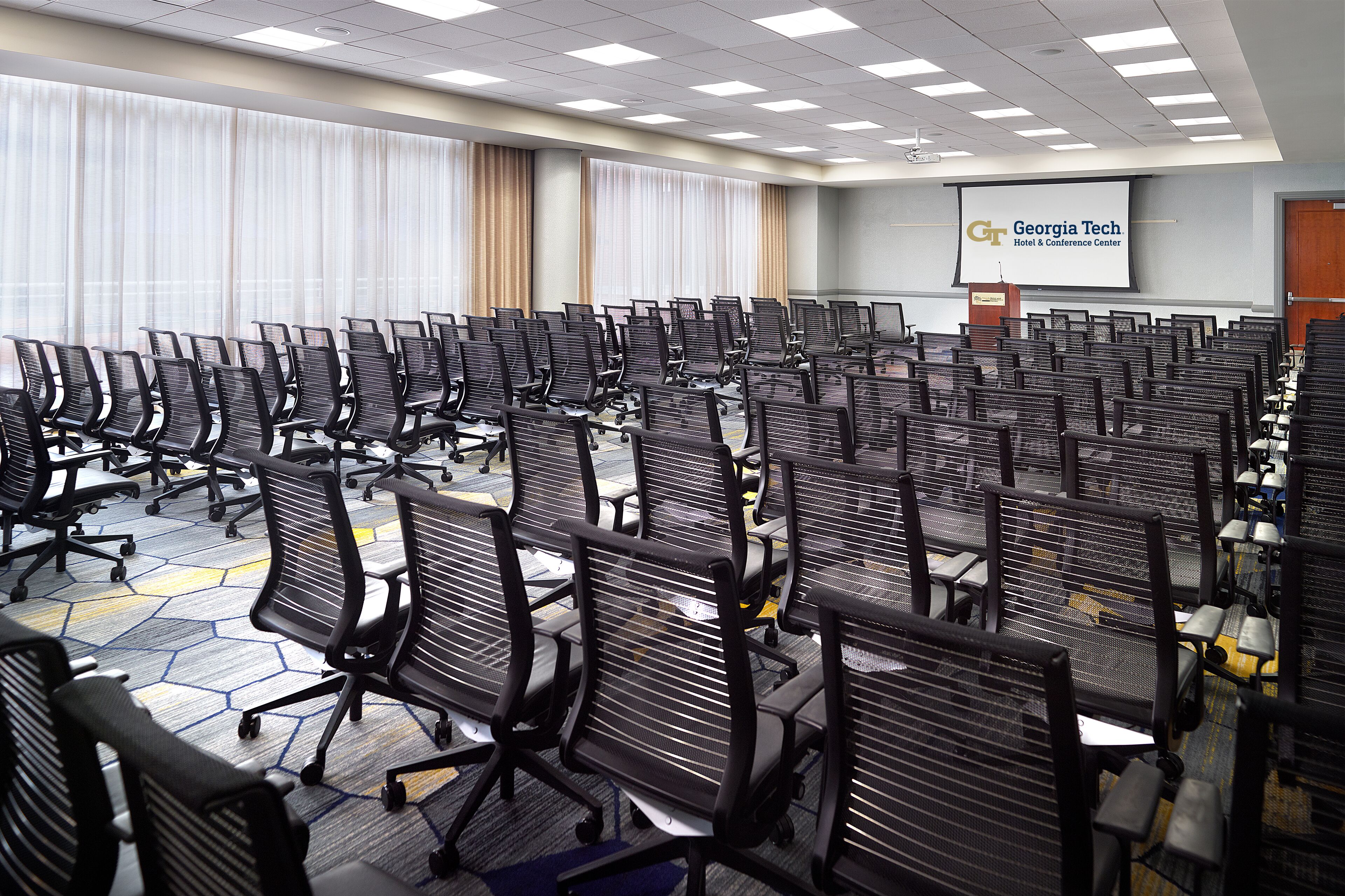 A conference room with rows of black office chairs, a projector screen displaying Georgia Tech logo, and a podium.