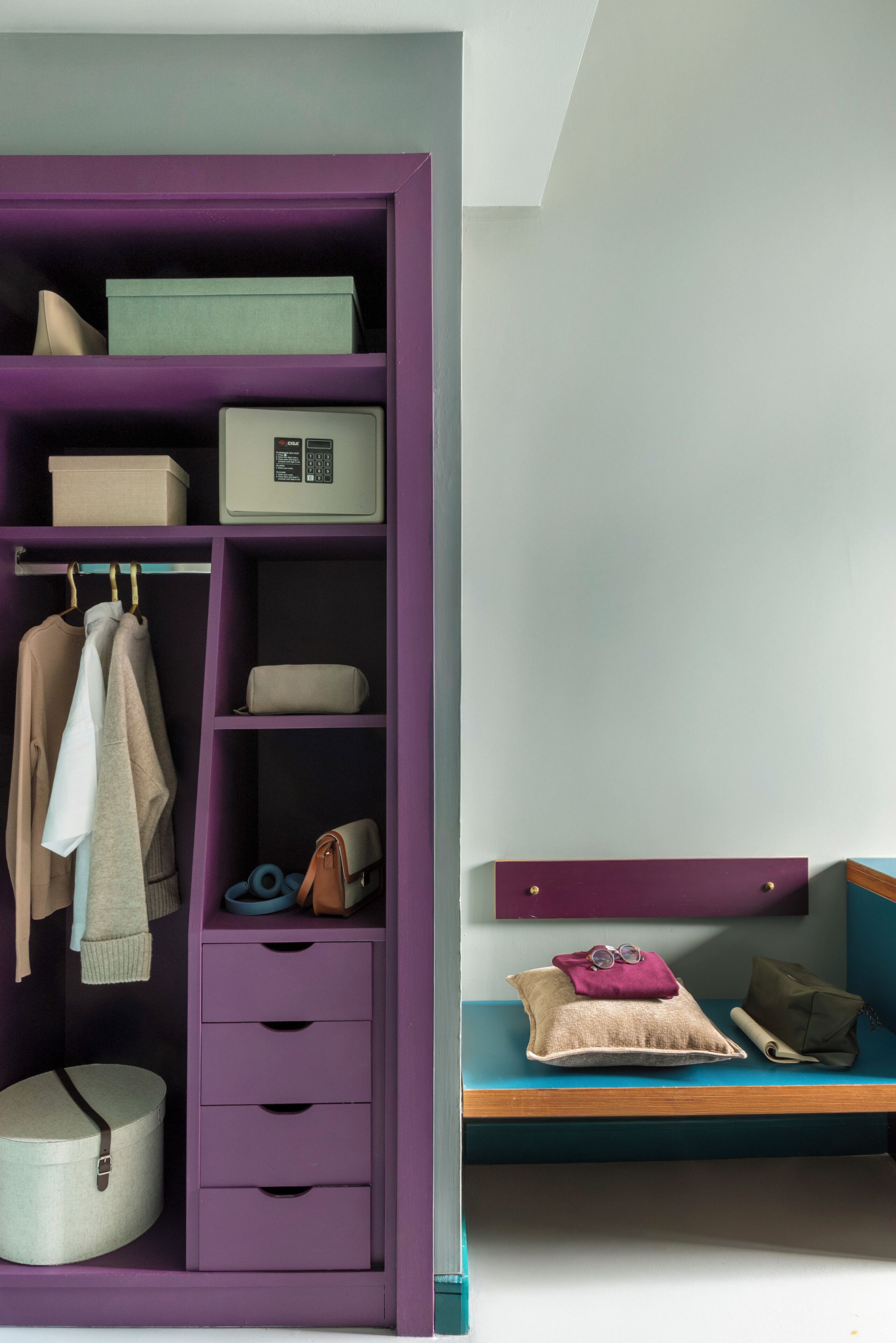 A room with a purple wardrobe, a teal bench, and a white wall.