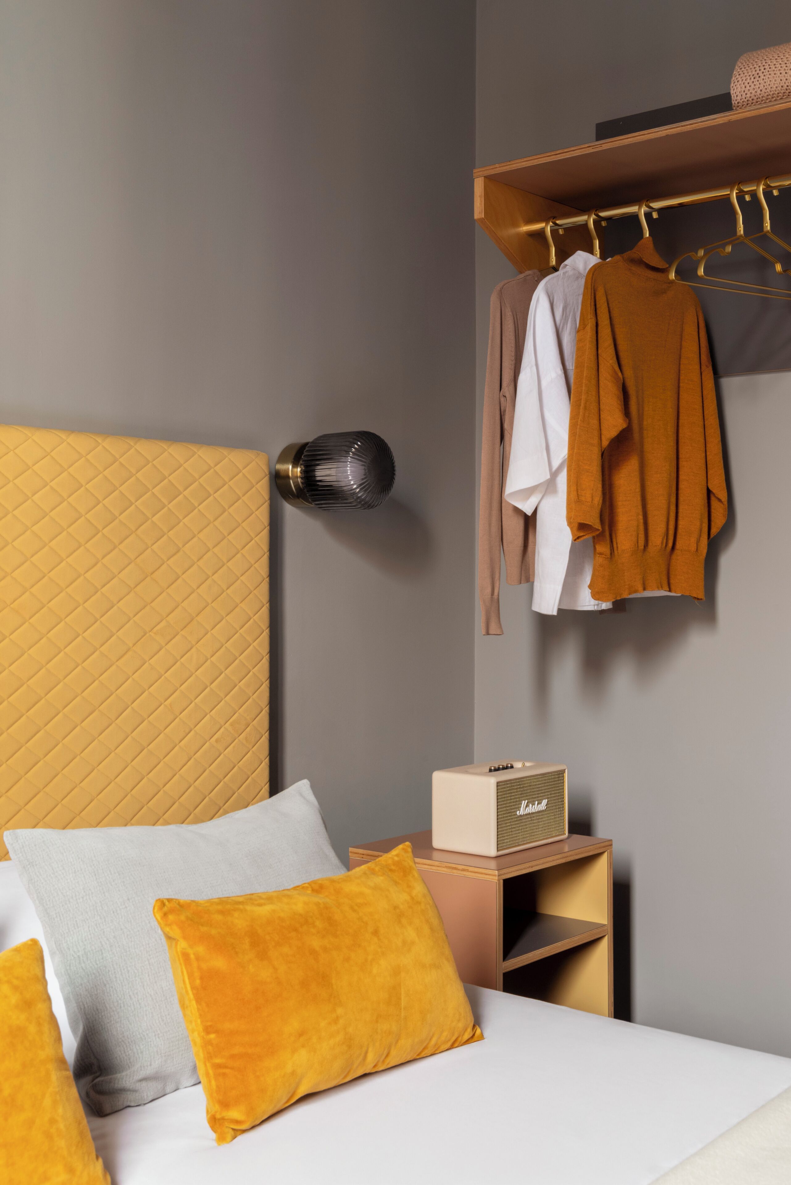 A bedroom with a bed, pillows, a nightstand, a radio, and a clothing rack.