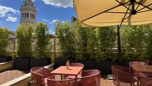 An outdoor patio with a table and chairs, a large umbrella, and a statue in the background. - Hotel Milani (Rome)