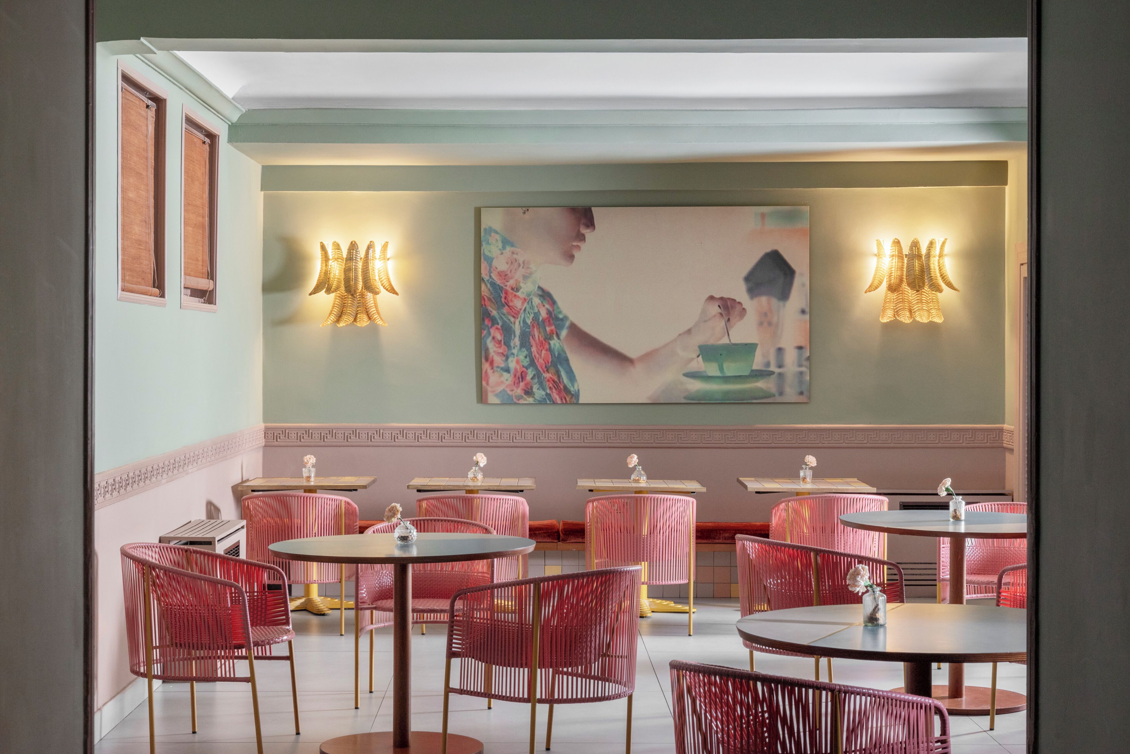 A restaurant interior with round tables, red chairs, and wall-mounted light fixtures.