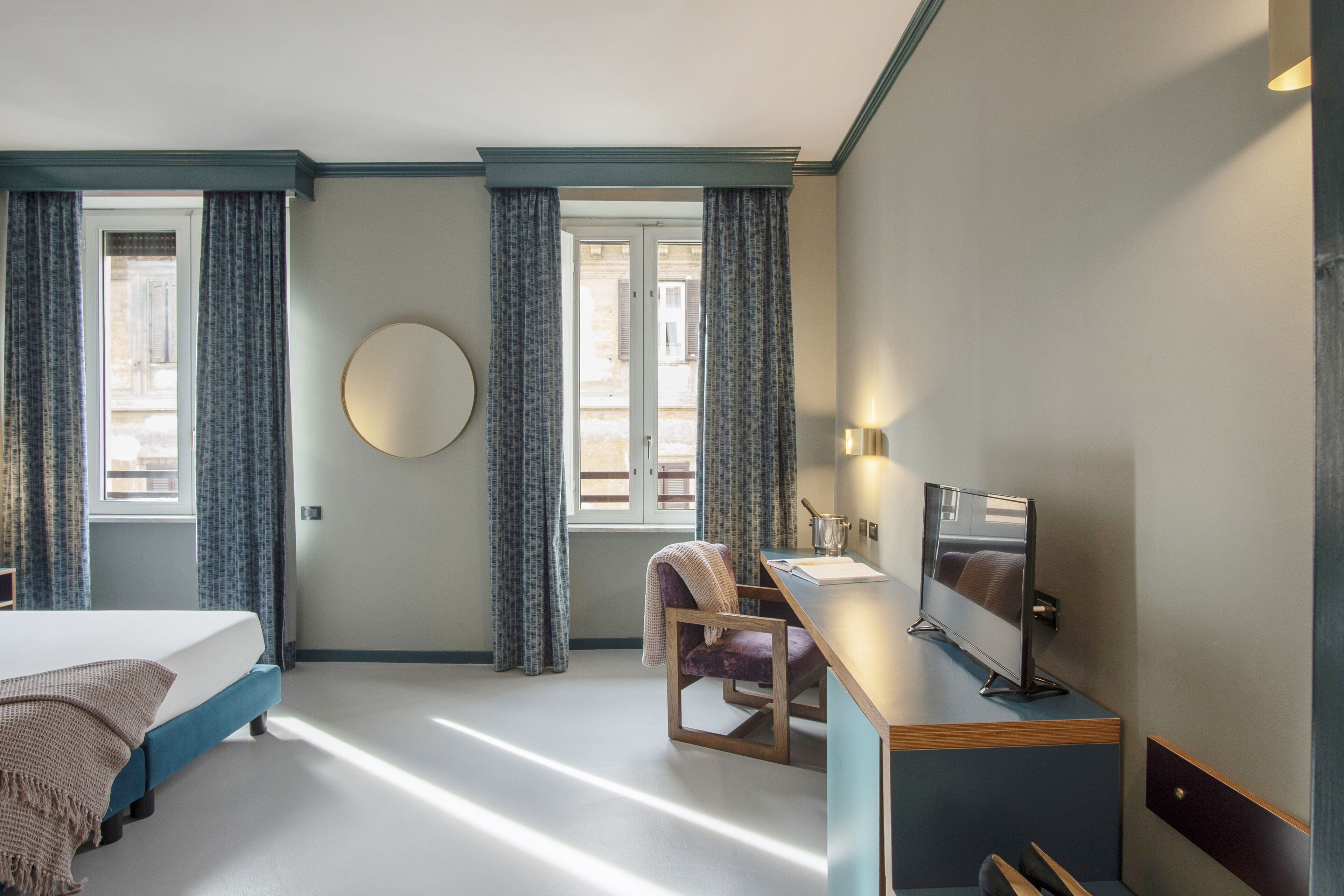 Habitación de hotel con una cama, un escritorio con computadora, una silla y un ventanal con cortinas.