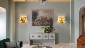 A room with a green sofa, a marble coffee table, a console table with decorative items, and a large landscape painting above the console. - Hotel Milani (Rome)