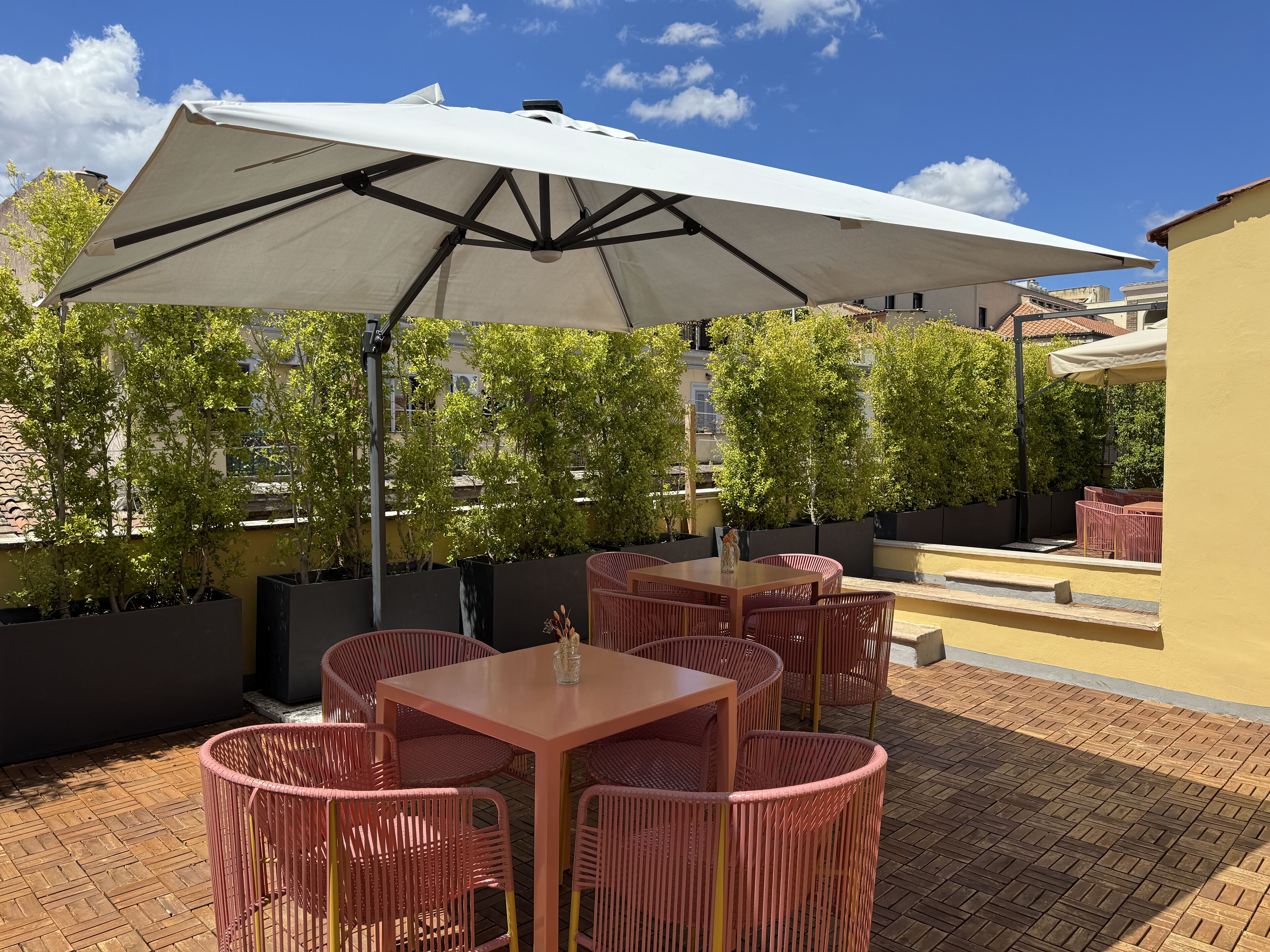 Ein Patio mit Sitzgelegenheiten im Freien, darunter Tische und Stühle, unter einem großen Sonnenschirm.