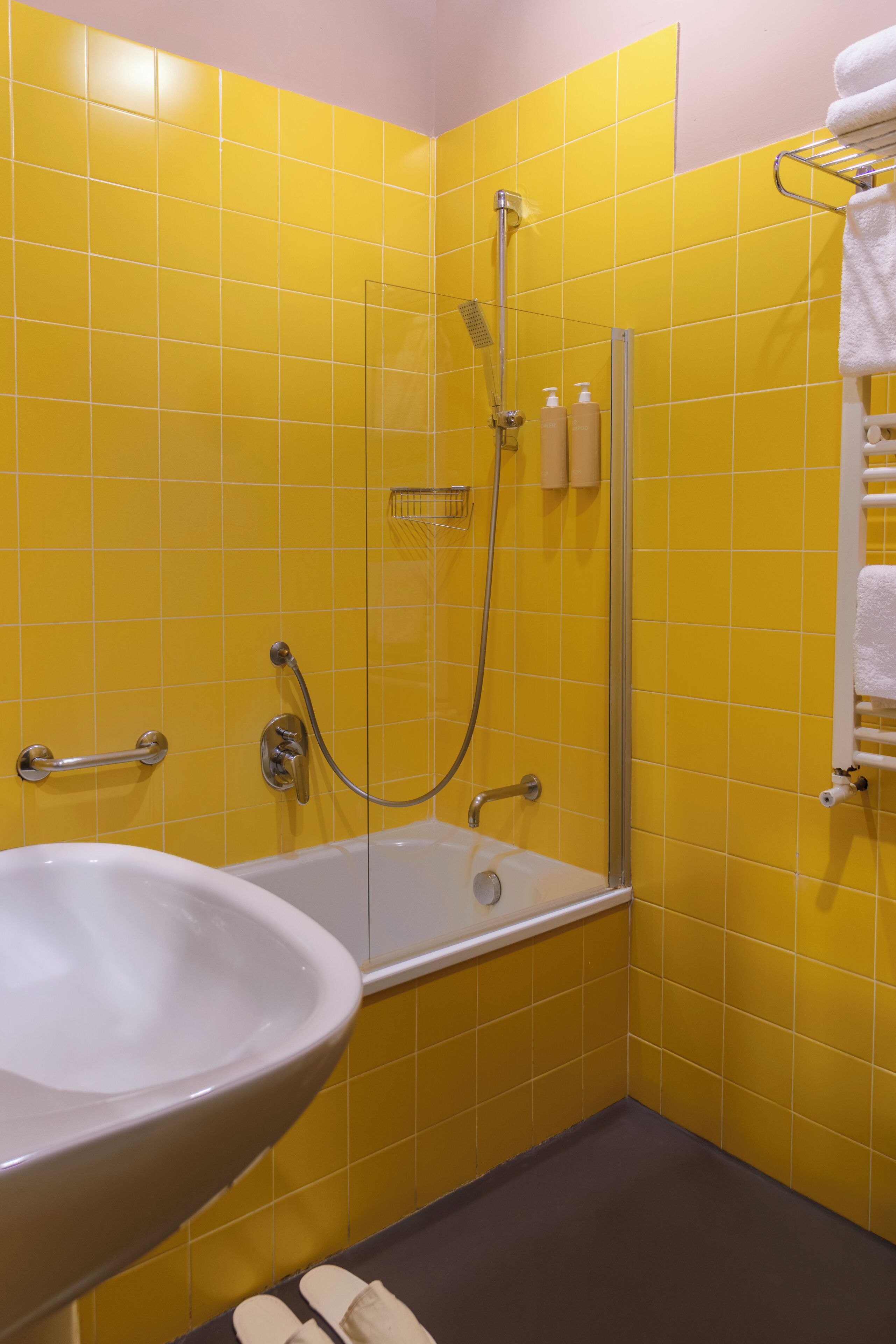A bathroom with yellow tiles, a glass shower enclosure, a white sink, and a towel rack.