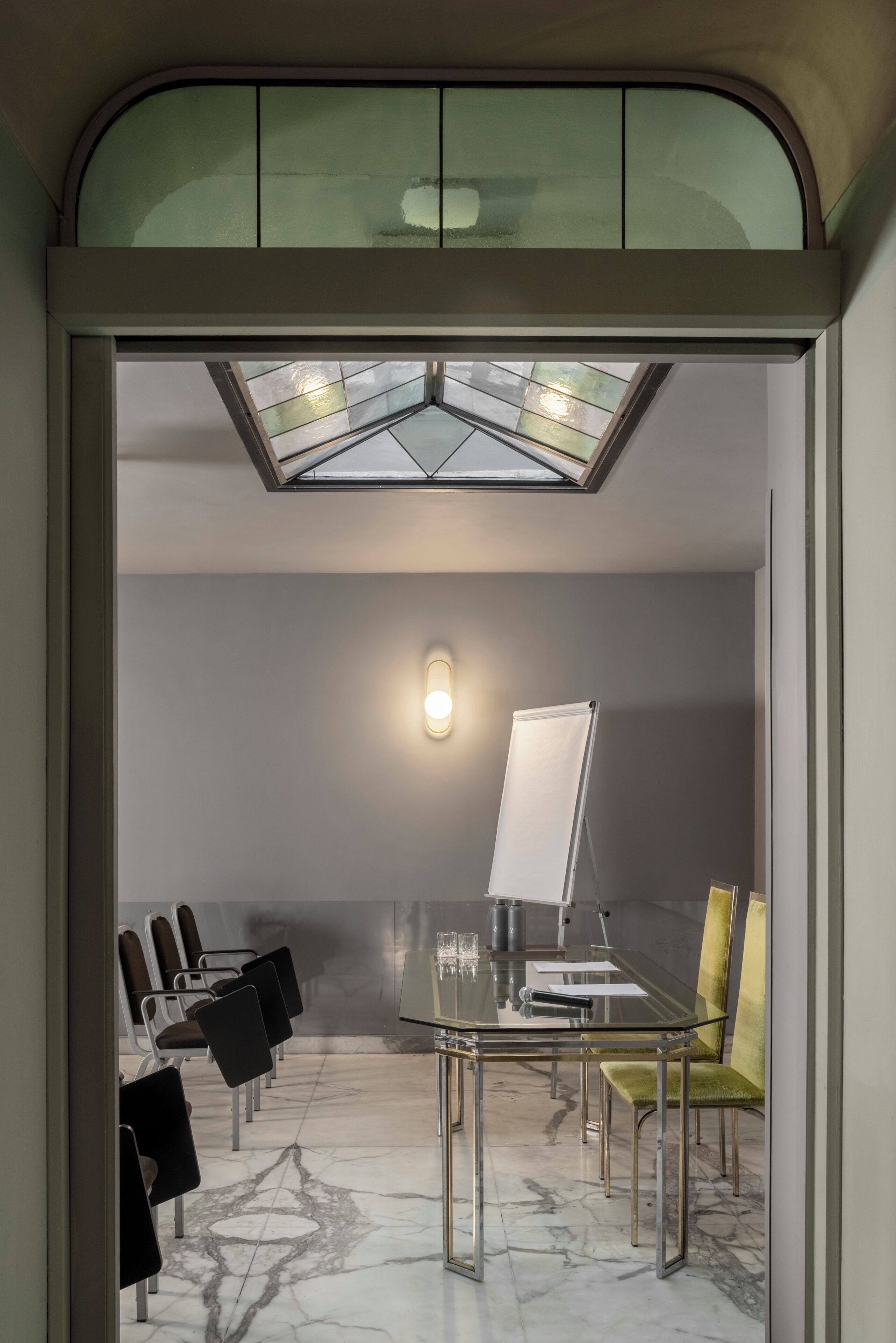 A conference room with a glass table, chairs, a whiteboard, and a skylight.