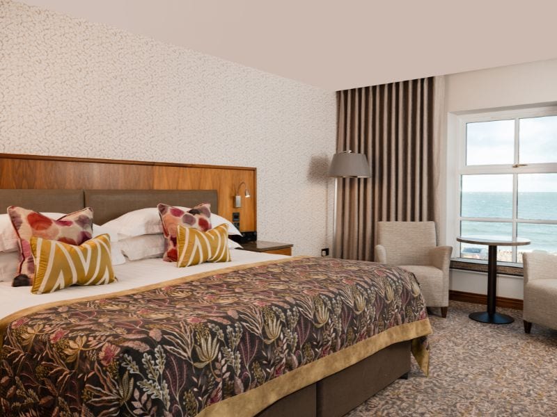 Habitación de hotel con una cama grande, una silla, una mesita y vista al mar.
