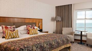 Habitación de hotel con una cama grande, una silla, una mesita y vista al mar.