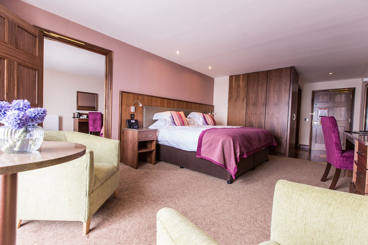 A hotel room with a bed, a desk, a chair, a mirror, and a round table.