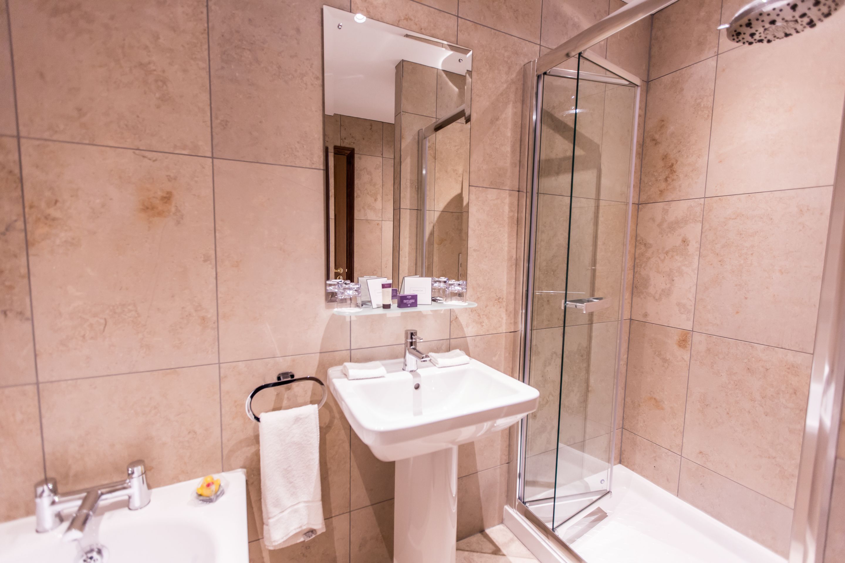A modern bathroom with a glass-enclosed shower, a pedestal sink, and a mirror above the sink.
