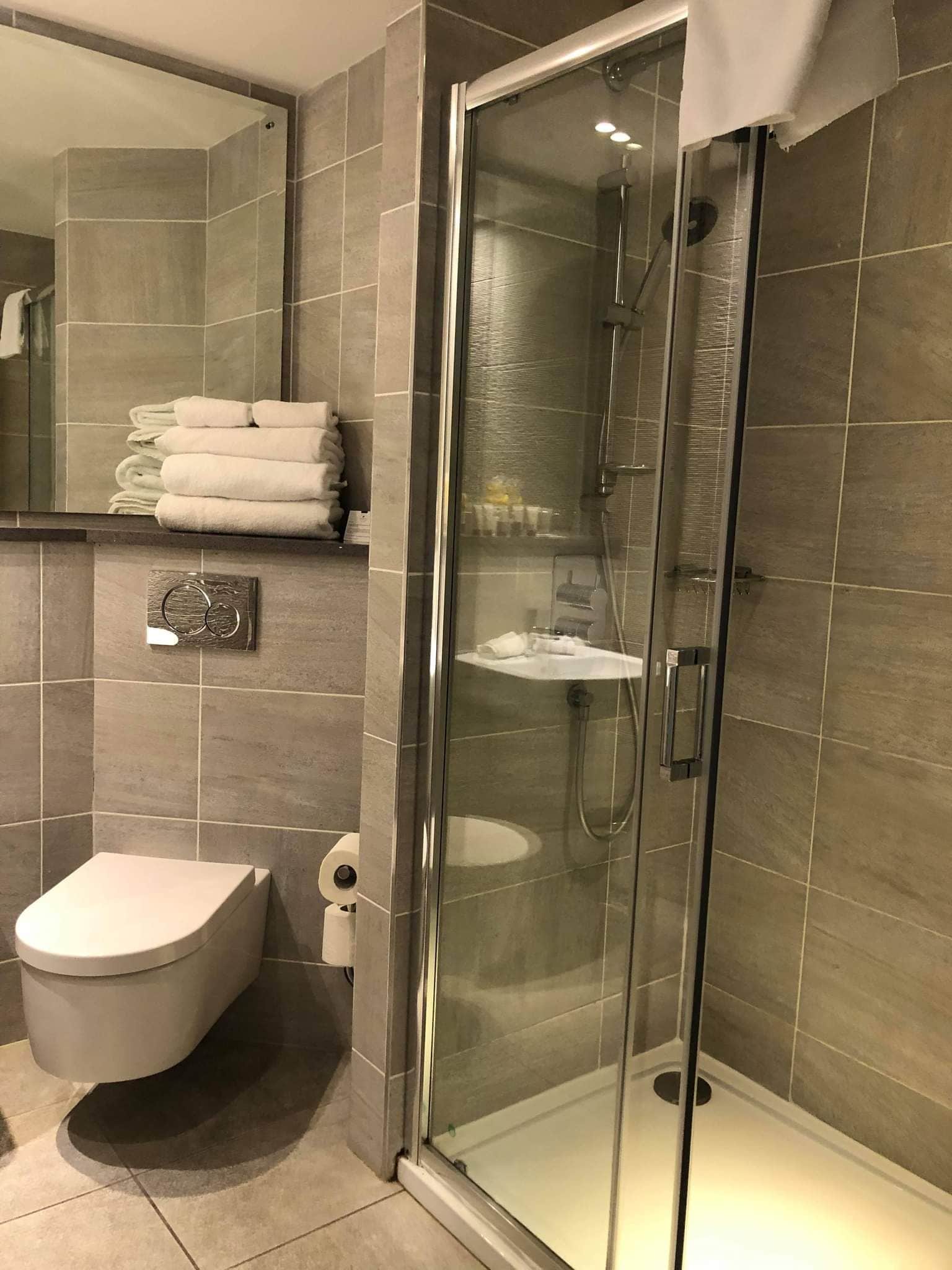 Un baño moderno con ducha envuelta en vidrio, inodoro y una pila de toallas dobladas con cuidado.
