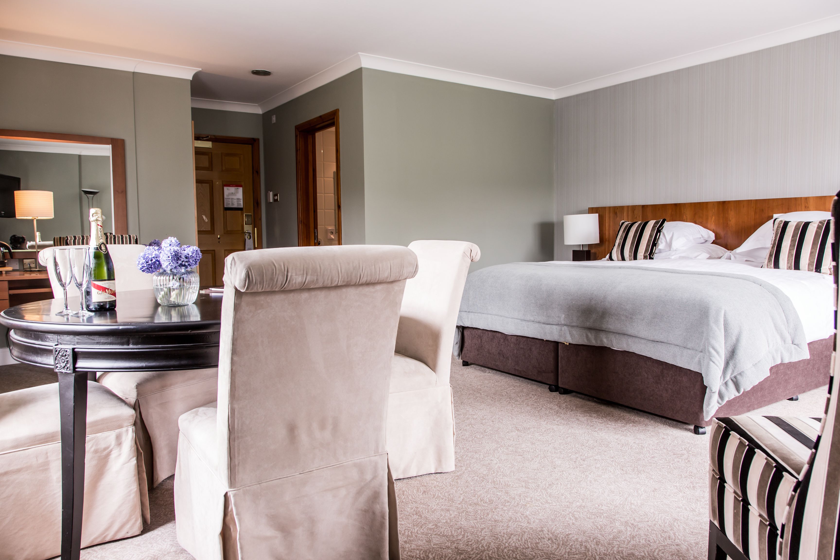 A hotel room with a bed, a sitting area with a table and chairs, a mirror, and a door.