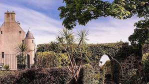 Un edificio histórico con una torre, un arco de piedra y un jardín con diversas plantas.