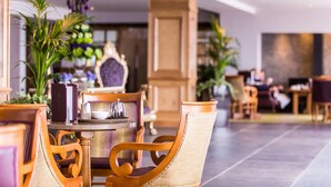 Un comedor interior bien iluminado con sillas de madera y una mesa redonda, rodeado de plantas en macetas y un espejo decorativo grande.