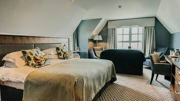 Habitación de hotel con una cama grande, un escritorio, una silla, un ventanal con cortinas y una alfombra estampada.
