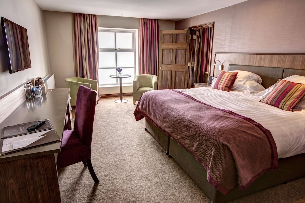 A hotel room with a bed, a desk, a chair, a small table, and a window with curtains.