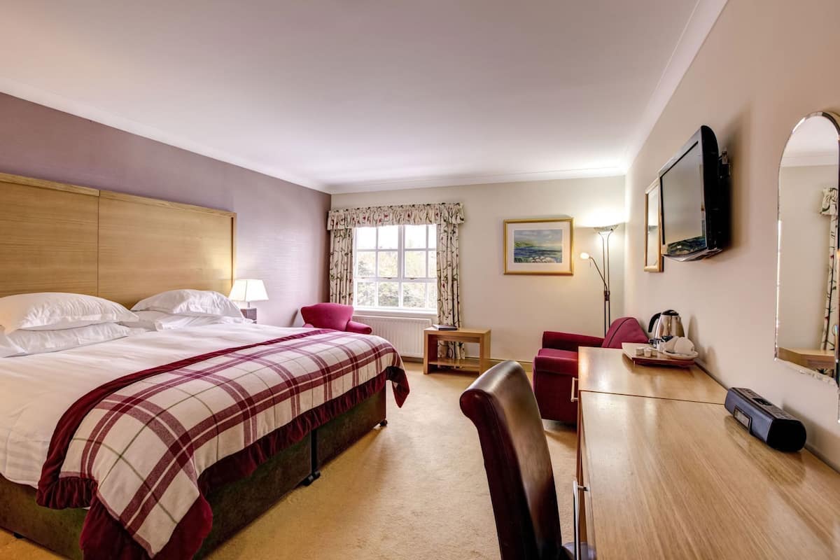 A hotel room with a bed, a desk, a chair, a TV, a window with curtains, and a painting on the wall.