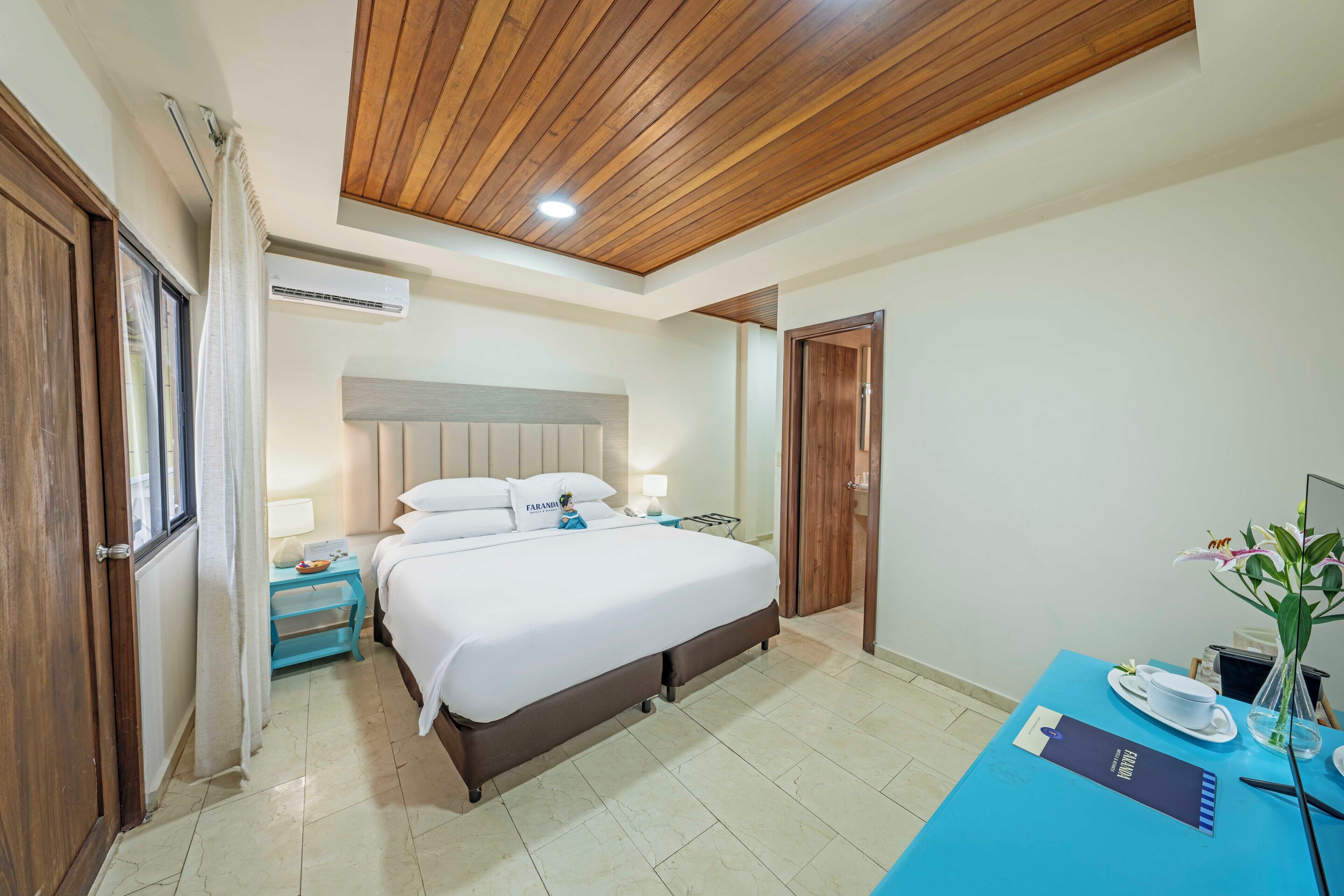 A hotel room with a bed, bedside table, nightstand, and a desk with a chair.
