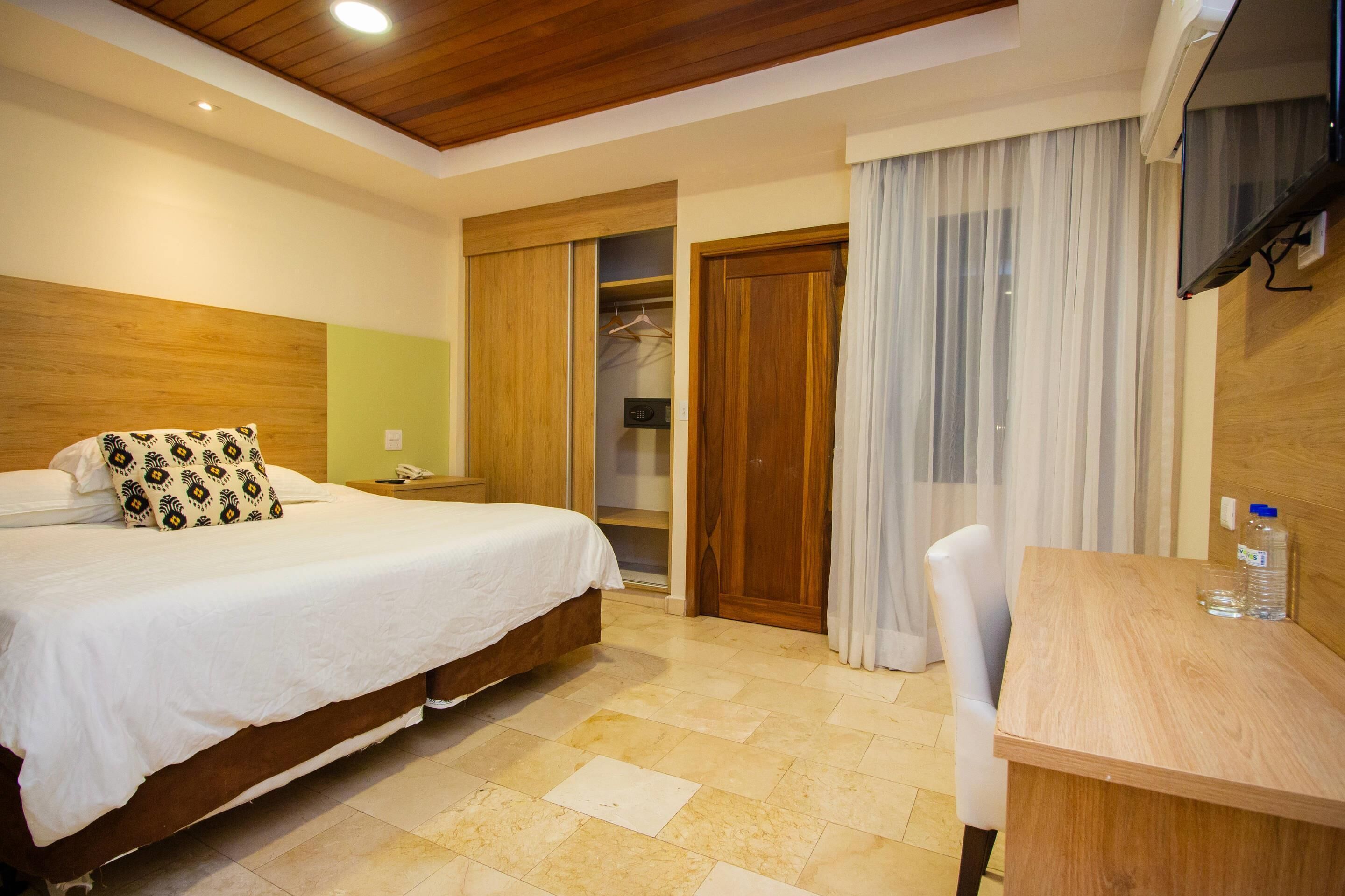 A bedroom with a bed, bedside table, wooden wardrobe, and a desk with a chair.