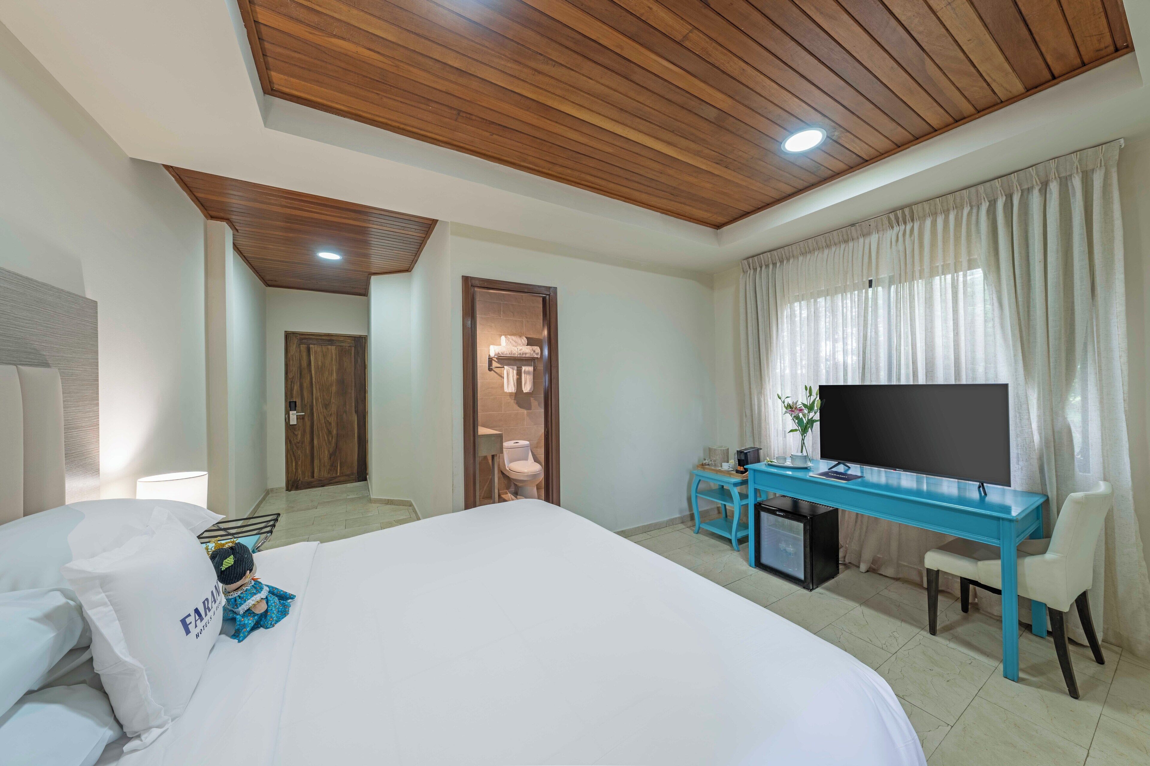 A hotel room with a large bed, a desk with a TV, and a bathroom visible through an open door.