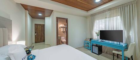 A hotel room with a large bed, a desk with a TV, and a bathroom visible through an open door.