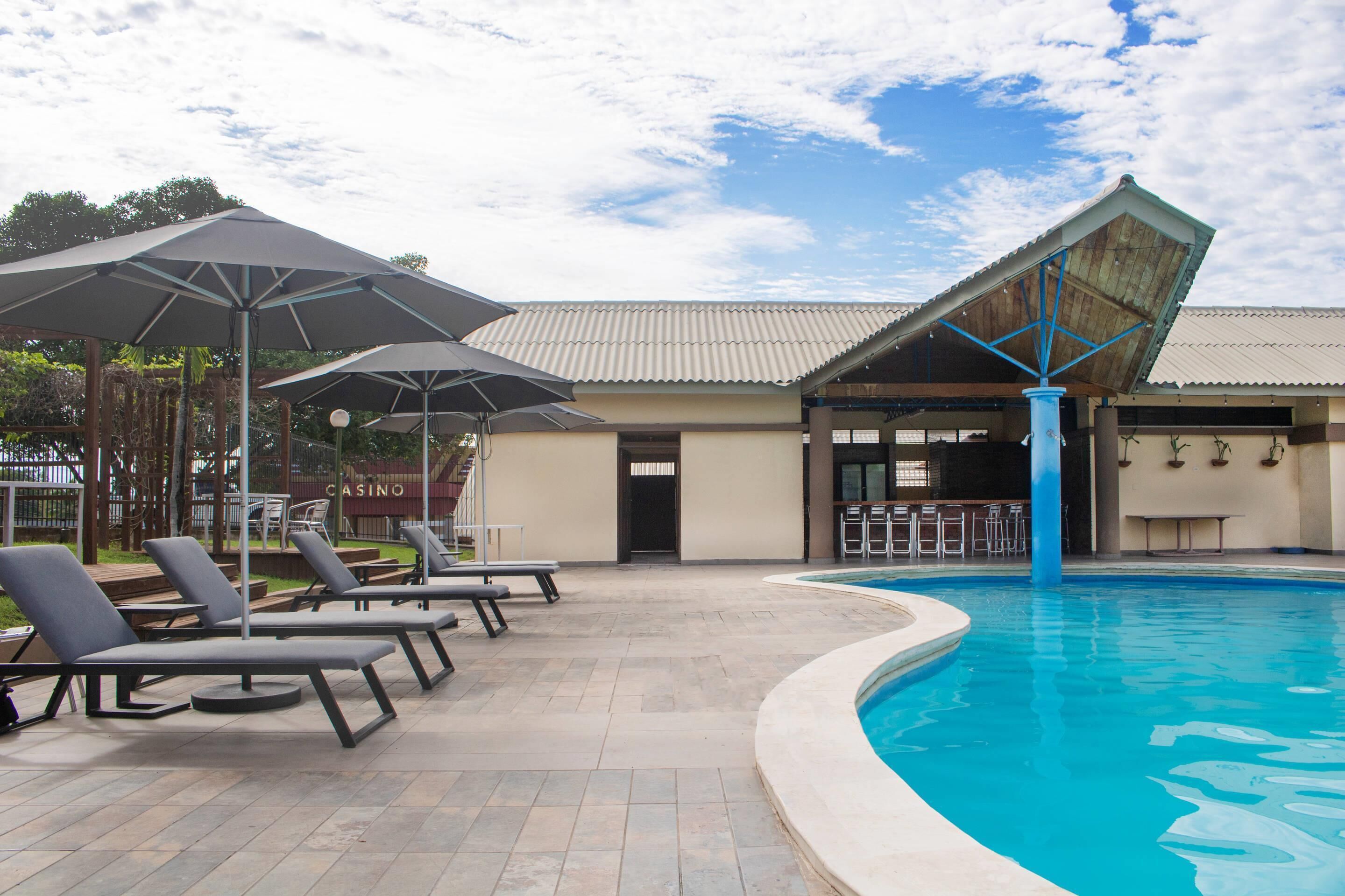 A swimming pool with lounge chairs and umbrellas, a bar area, and a building with a tiled roof.