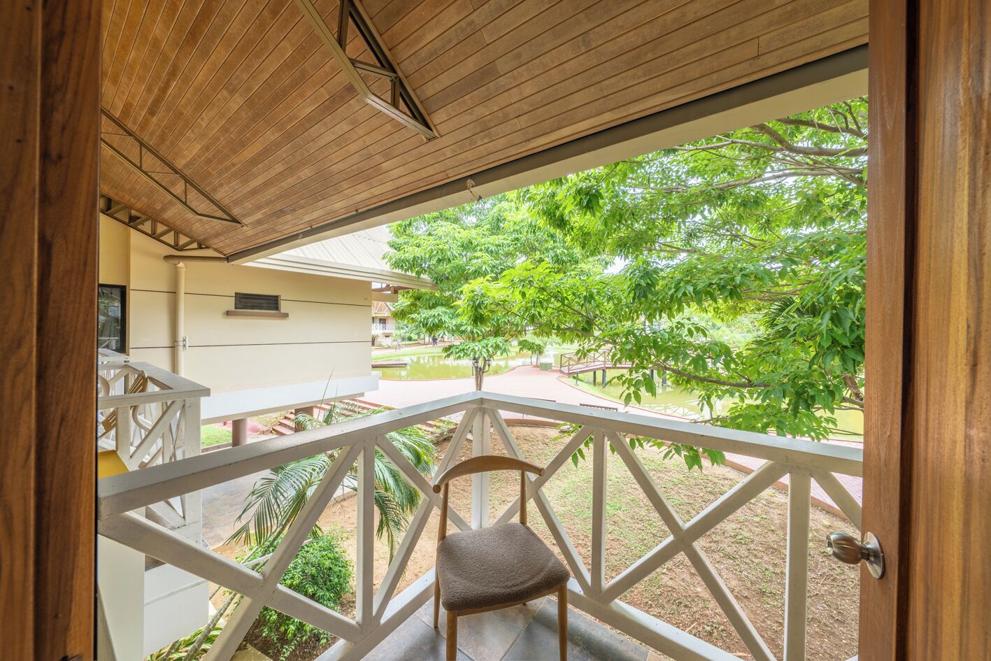 Een houten balkon met een witte railing, een stoel en uitzicht op een tuin met bomen en een pad.