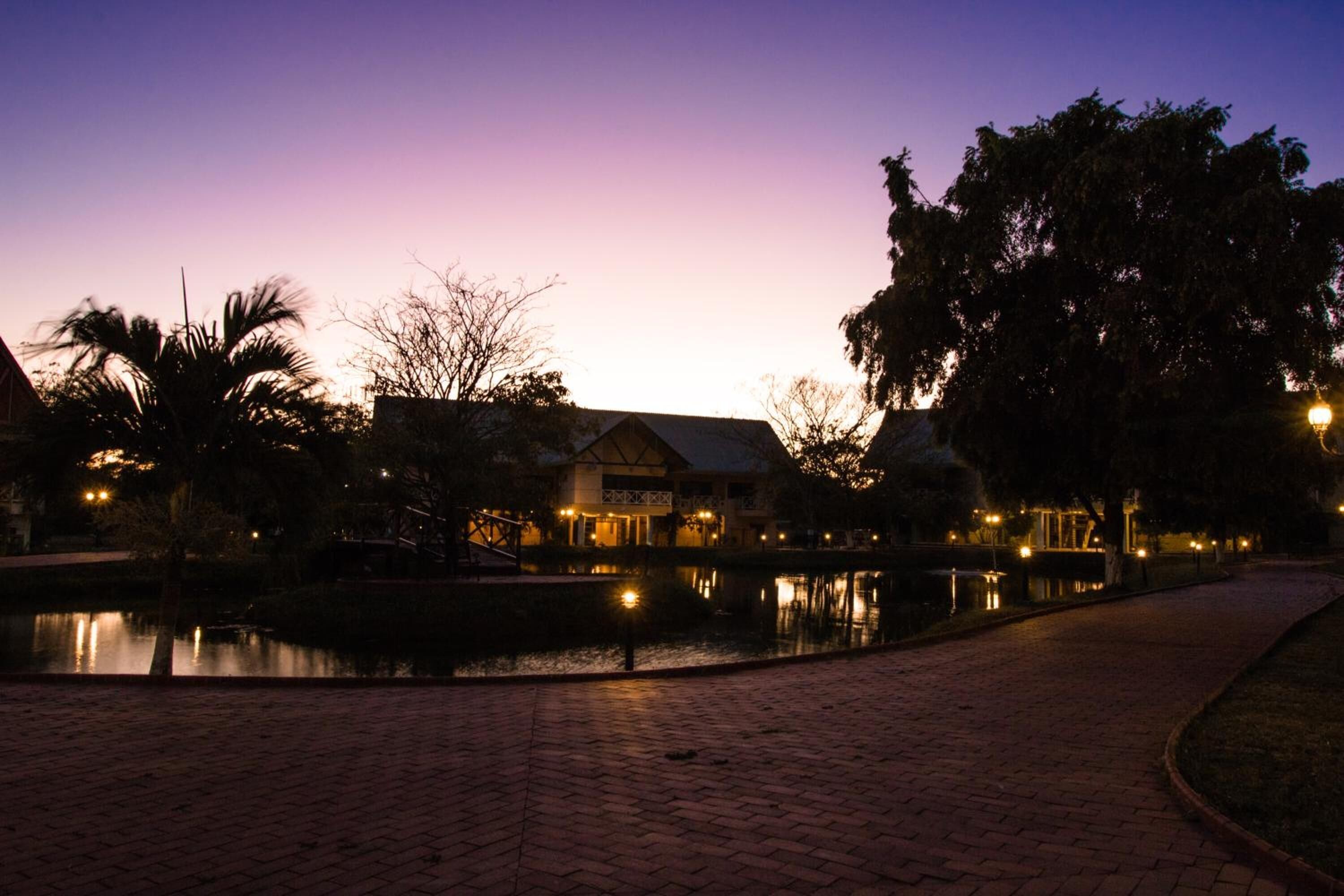 A paved walkway beside a calm body of water, with a building featuring a sloped roof and a visible porch area.