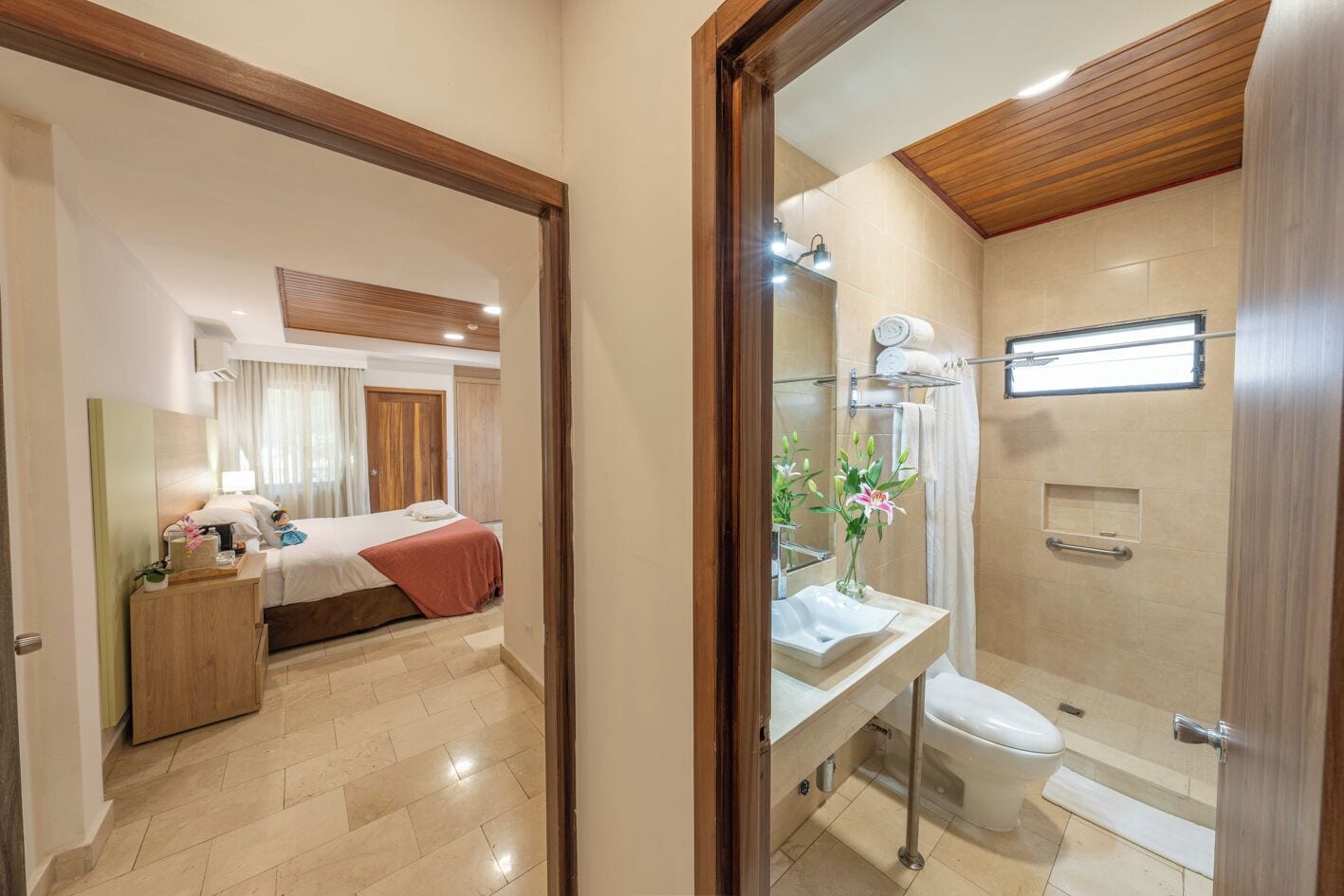 A hotel room with a bed, bedside table, and a bathroom with a shower, toilet, and sink.